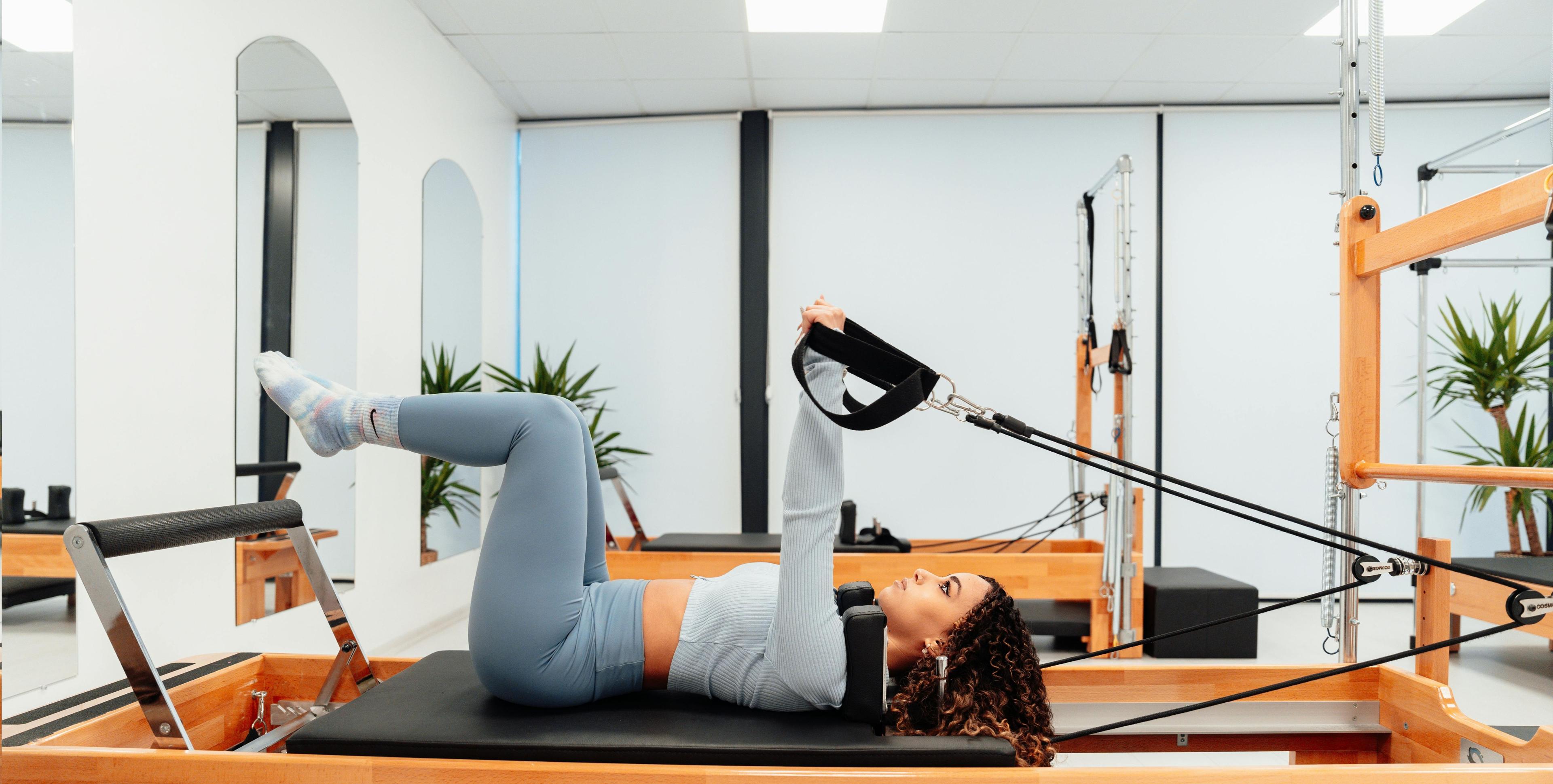 Woman using a pilates reformer machine in a well lit studio.